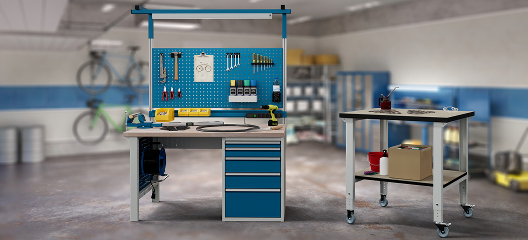 Zwei Werkbänke in Baukastenbauweise in einer Hobbywerkstatt, eine mit Systemaufbau und einem Fahrradreifen auf der Arbeitsplatte, daneben eine mobile Werkbank mit Ablageboden und Utensilien.