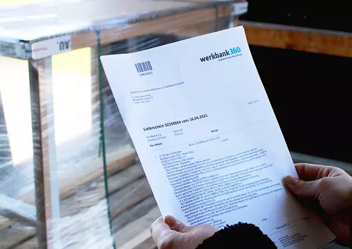 Eine Person hält ein Lieferdokument von werkbank360 vor dem Hintergrund einer Werkbank mit einer durchsichtigen Schutzplane.