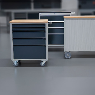 Werkzeugwagen, Montagewagen und eine Rollwerkbank, ausgestattet mit Schubladen und rolladen, nebeneinander platziert, in einem industriellen Arbeitsraum.