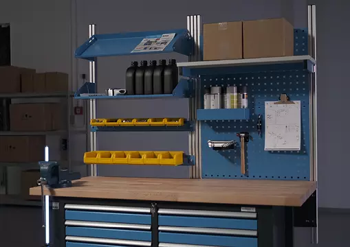 Voll ausgestattete Werkbank mit blauem Systemaufbau, Schubladen und Werkzeugablage in einem Lagerbereich.