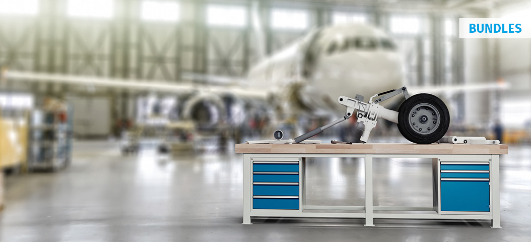 Schwerlastwerkbank mit Schubladenschränken in einer Flugzeughangar-Umgebung, bestückt mit einem Fahrwerksbauteil zur Wartung oder Montage in der Luftfahrttechnik.