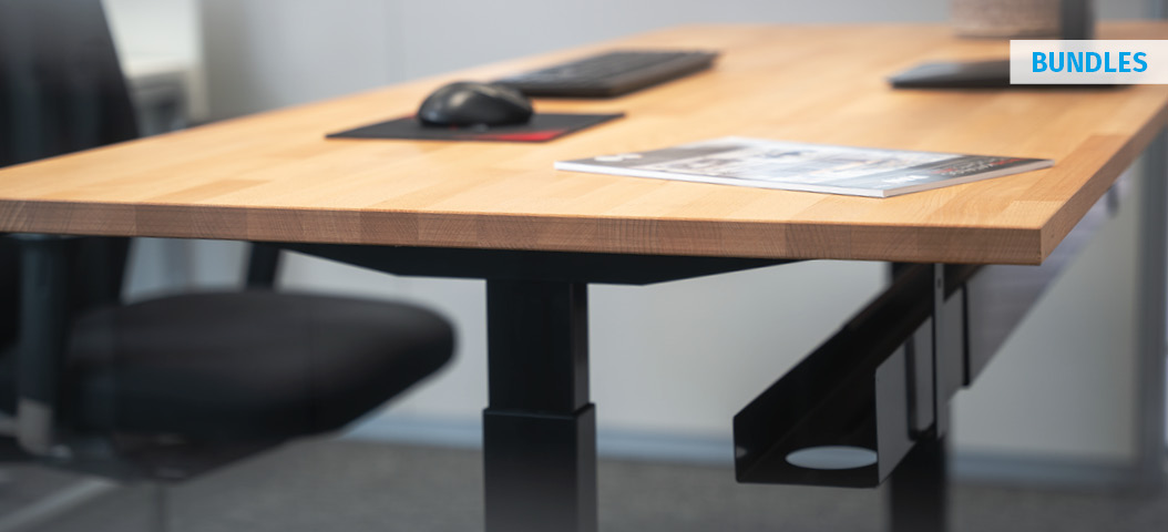 Nahaufnahme des elektrisch höhenverstellbaren Schreibtischs adlatus 100 mit massiver Buche-Massivholzplatte, schwarzem Gestell und Kabelmanagement im modernen Büro, ausgestattet mit Monitor, Tastatur und Maus.