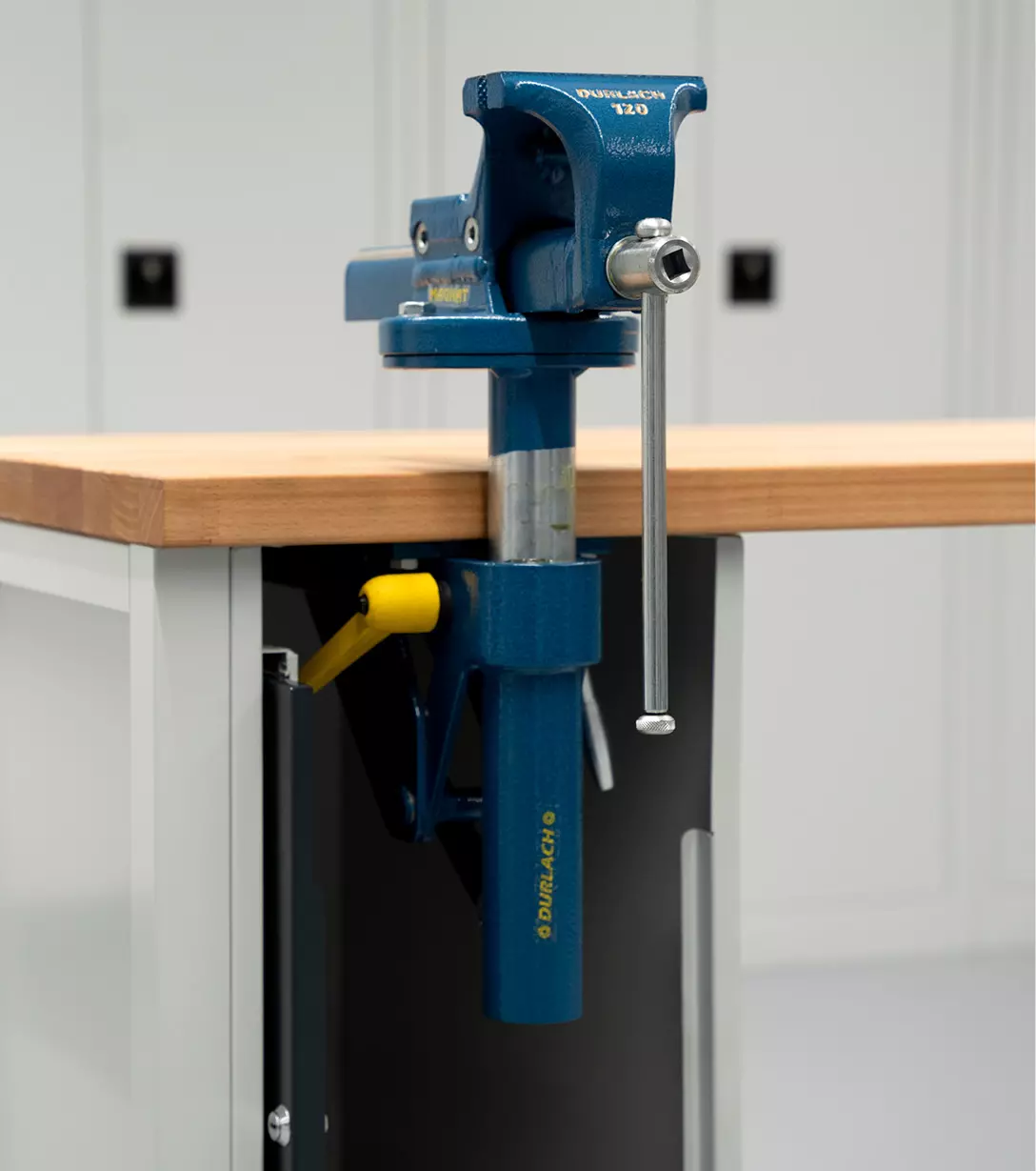 Höhenverstellbarer Schraubstock in Blau, montiert an einer Werkbank mit Holzplatte.