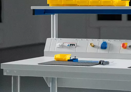 Ein Arbeitsbereich mit einer Melamin-Arbeitsplatte, darauf ein Messwerkzeug und eine gelbe Kunststoffbox, mit einer Energieversorgungseinheit im Hintergrund.
