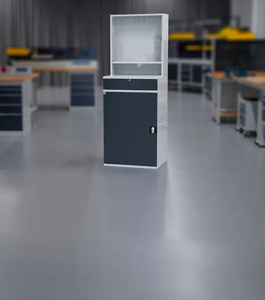 Computerschrank in Weiß und Anthrazit in industrieller Umgebung mit Werkbänken im Hintergrund.