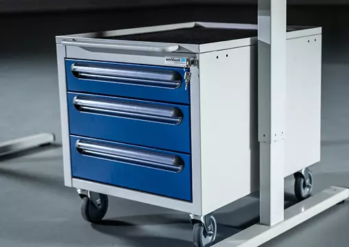 Fahrbarer Unterbau-Container in Weiß mit drei blauen Schubladen, ausgestattet mit Rollen, neben einer Werkbank.