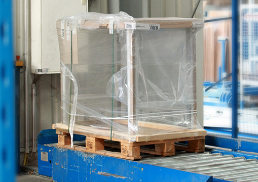 Verpackter Artikel auf einer Holzpalette, bereit für den Versand, auf einer blauen Fördereinrichtung.