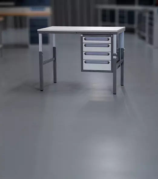 Arbeitstisch der Serie E mit integrierten Schubladen und heller Arbeitsplatte in industrieller Umgebung.