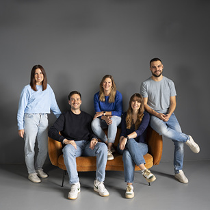 Gruppenbild: Team werkbank360 gemeinsam vor einem grauen Hintergrund, drei sitzend und zwei stehend.