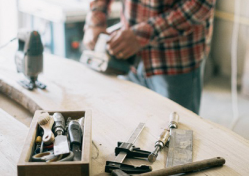 Handwerker im Hintergrund, der Holz in einer Werkstatt bearbeitet.
